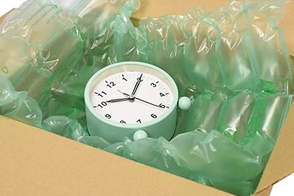 A mint green alarm clock packed in a cardboard box with a green air pillow cushioning.