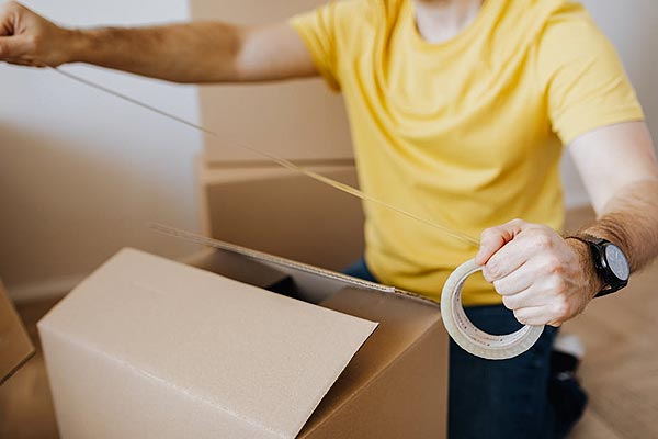 Close-up shot of a man putting tape on a cardboard box. 