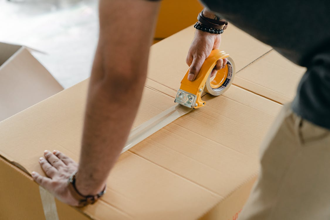 Close-up of a man closing a cardboard box with tape.