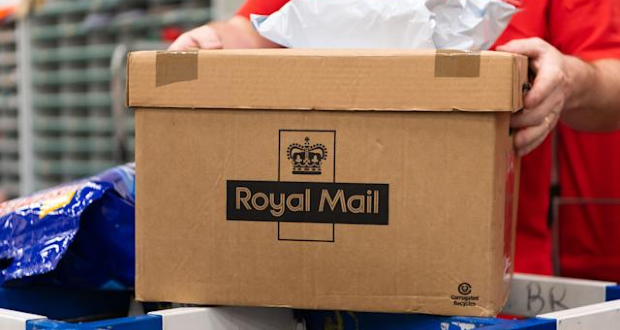 Person in red clothing holding a Royal Mail-branded cardboard shipping box.